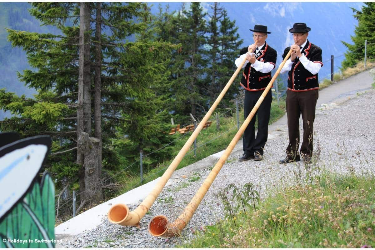 Two men in traditional Swiss costumes playing Alphorns