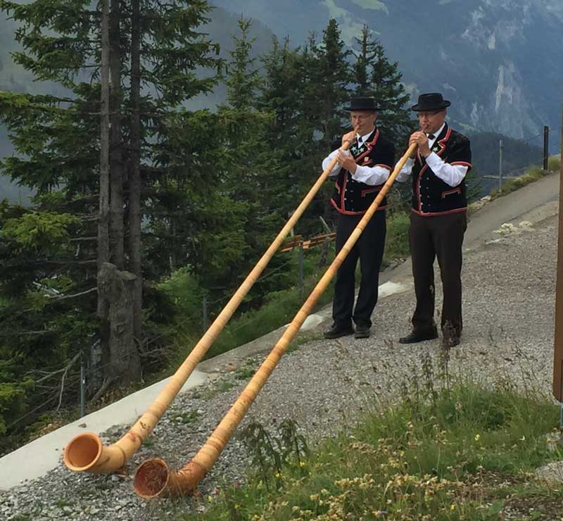 Two mean in traditional Swiss costumes playing Alphorns