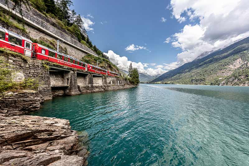 Bernina Express train passing by Lago Bianco in Switzerland