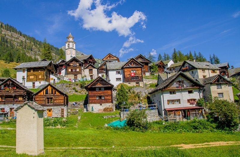 Wooden houses dot the hillside of Bosco Gurin, Switzerland with the church tower in the background