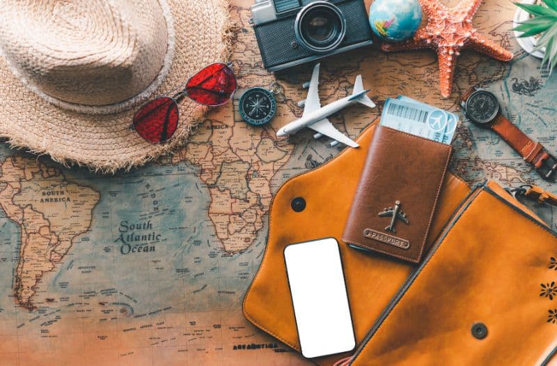 Essential travel items including passport, hat, sunglasses, camera and phone on a map of the world