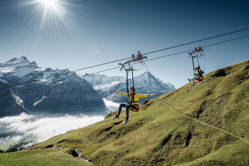 Two people riding the First Flyer Grindelwald zip line.