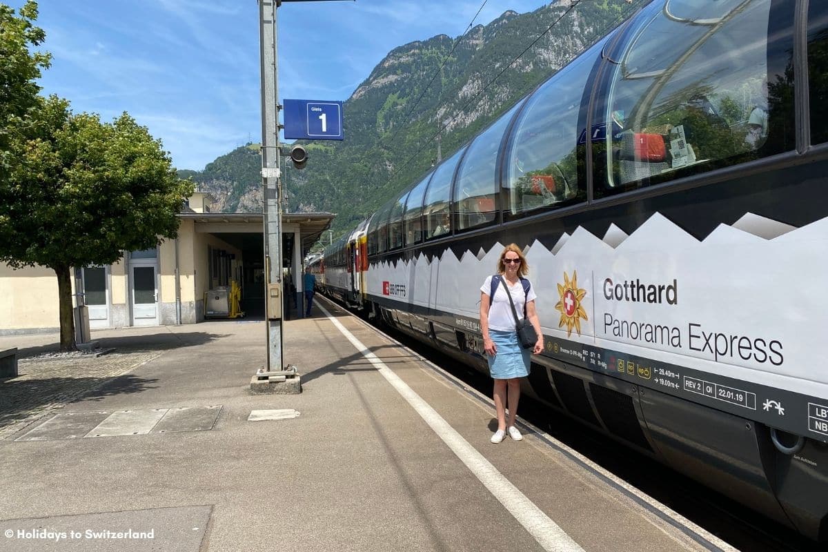 Woman standing beside Gotthard Panorama Express train.