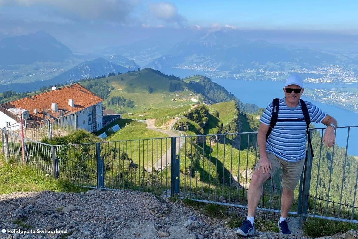 Man standing on hiking trail with a view of Lake Lucerne behind him.