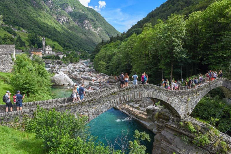 Crowds of tourists walking over Lavertezzo's double-arched bridge.