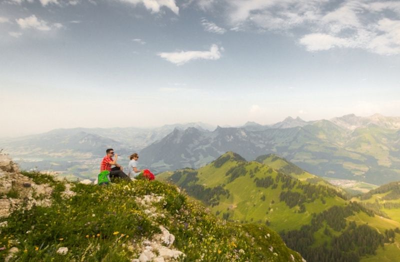 A man and a woman sit on the top of Mt. Moleson looking towards the Pre-Alps.