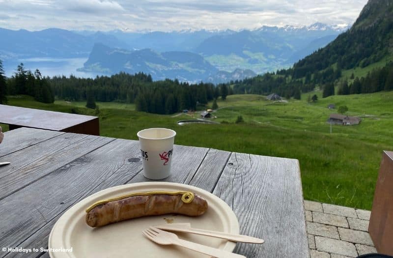 Sausage on a plate and a coffee cup on a wooden table at Mt. Pilatus overlooking Lake Lucerne