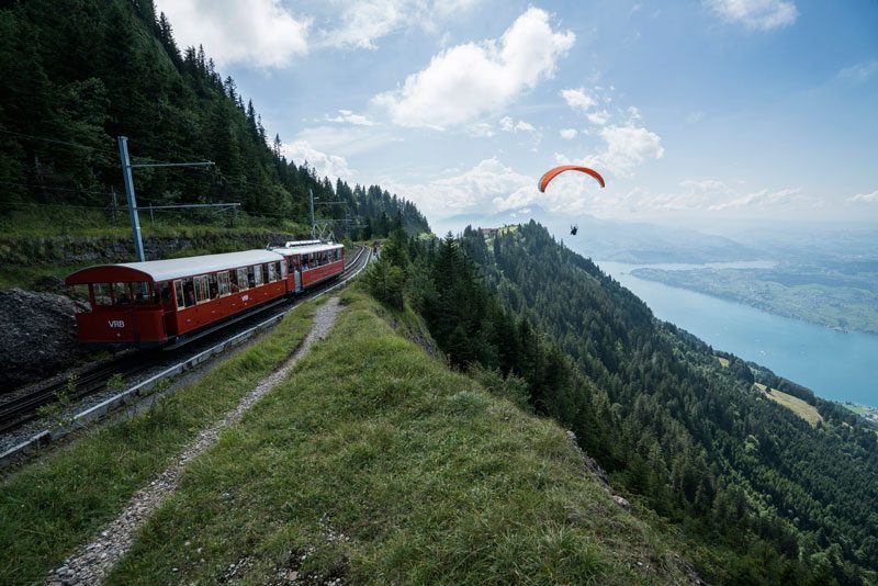 A paraglider flies over Mt. Rigi as the Rigibahn cogwheel train passes by.