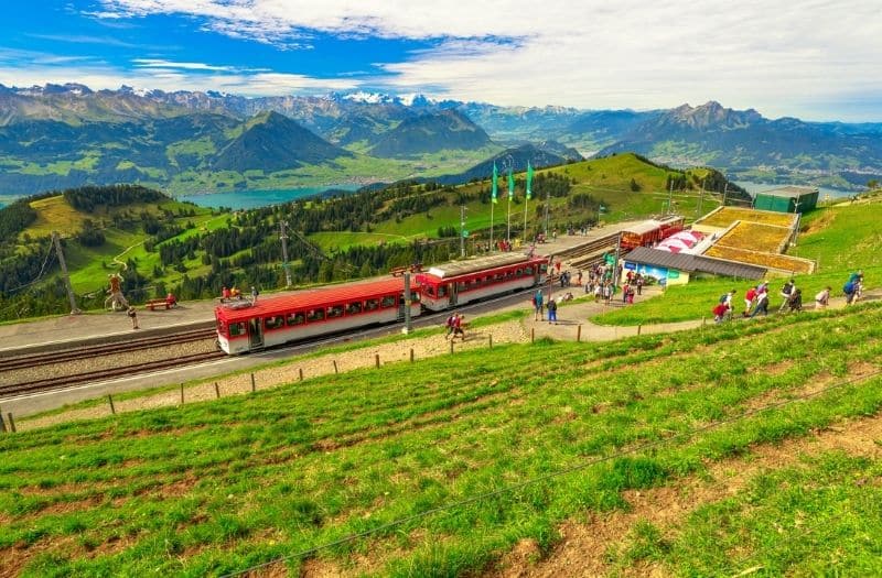 Mt. Rigi cogwheel train at Rigi Kulm station with a panoramic view of lakes and Alps.