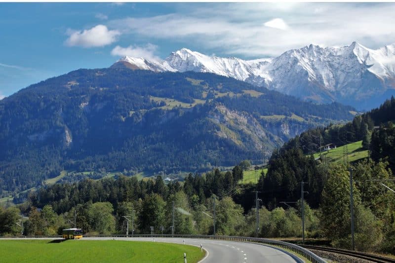 A bus travelling on a road in Switzerland with snow covered mountains in the distance