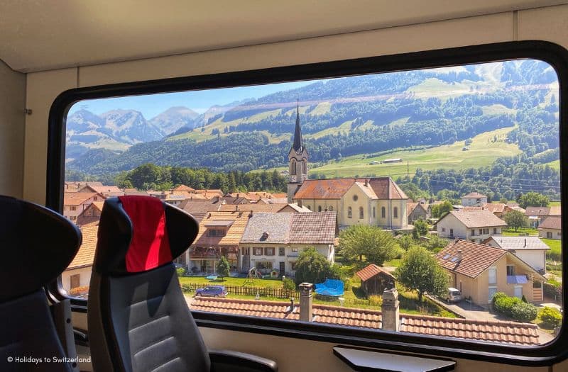 A picturesque Swiss village can be seen from the window of a passing train.