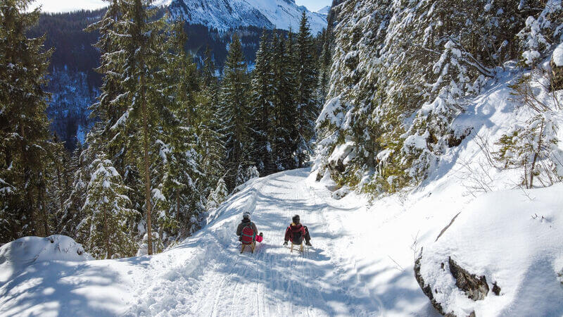 Two people sledding on a snowy trail.