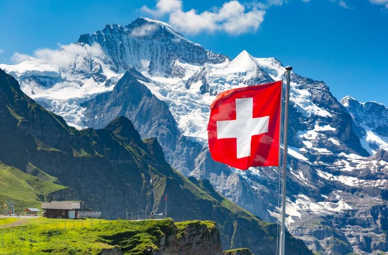 Swiss flag with view to snow capped Swiss Alps at Mannlichen