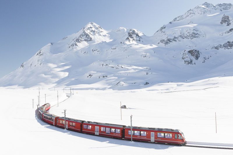 A red train passing through a snowy landscape in Switzerland