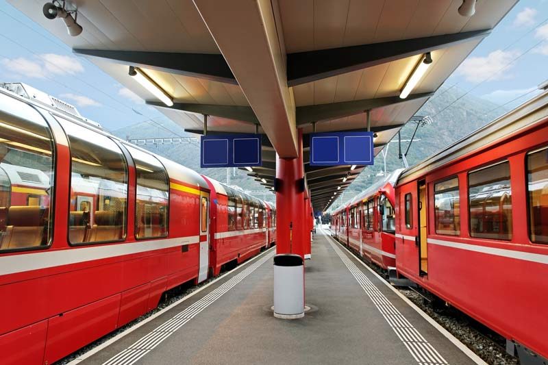 Two trains wait at a station platform in Switzerland.