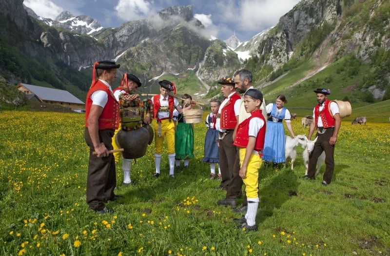 Children and Alpine herdsmen wearing traditional costume gather on an alpine pasture with Mt. Santis is the background.