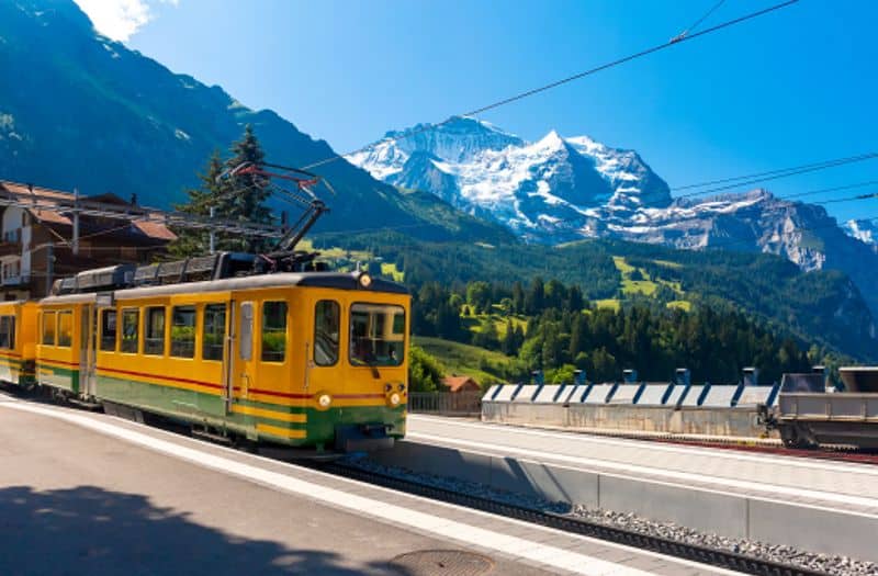 Train at Wengen station in Switzerland with snow capped mountains in the distance