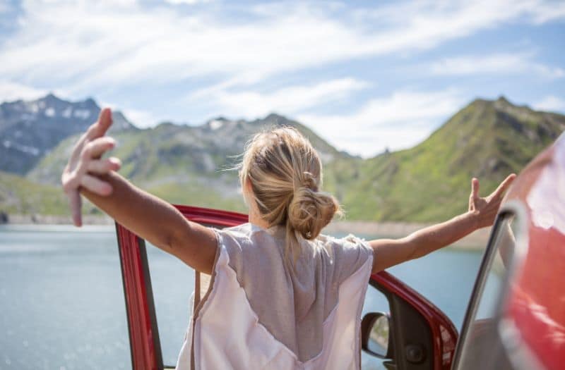 Woman with arms outstretched next to car beside a Swiss lake